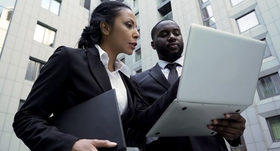 one african american woman in a dark suit and white shirt is pointing at a laptop and speaking with an african american man in a dark suite and tie