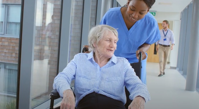 Young healthcare professional pushing an older woman in a wheelchair down a hallway