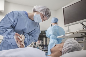 female healthcare worker in blue surgery scrubs holding the hand of a male patient laying down on a table