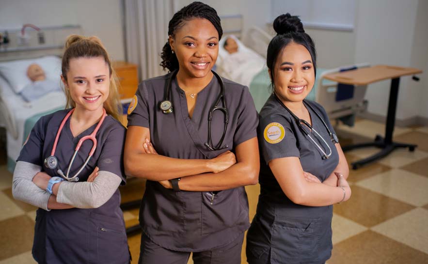 three nursing students in South University scrubs standing side by side in a classroom