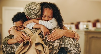 man in a military uniform wearing a backpack hugging 2 kids, one boy and one girl