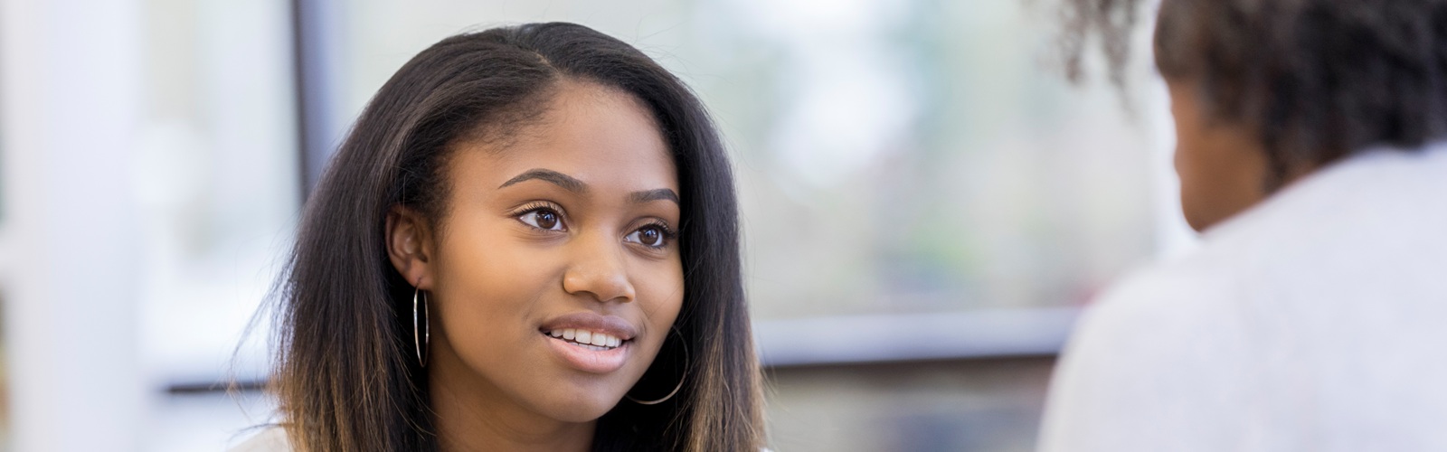 young african american woman in a white sweater sitting on a couch speaking to another person
