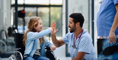 small female child in a wheelchair high fiving with a male nurse