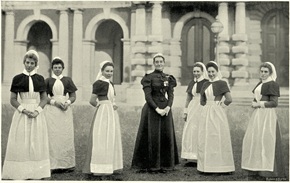 seven women in early 1900 nursing uniforms standing together outside of a hospital