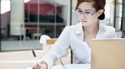 Female accountant at desk writing in front of laptop-alt-text