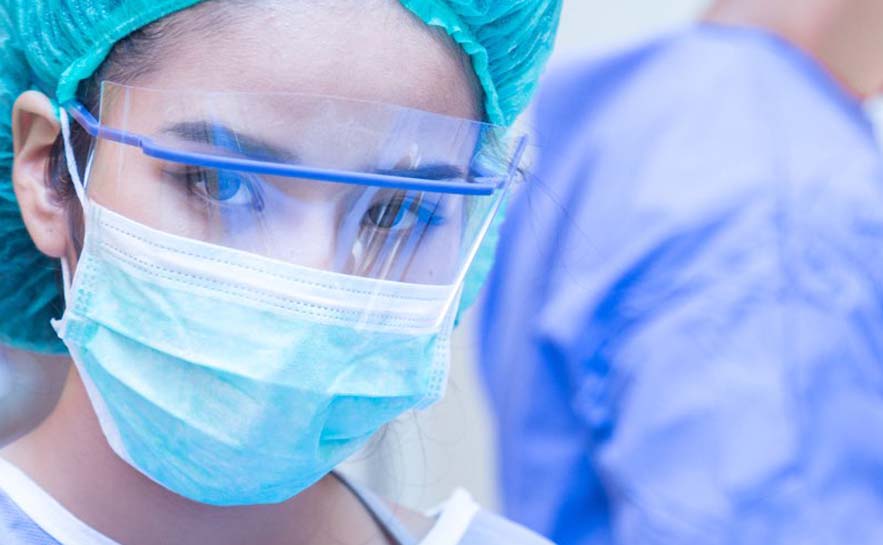 Person wearing a surgical cap and mask, with another person in blue scrubs in the background.