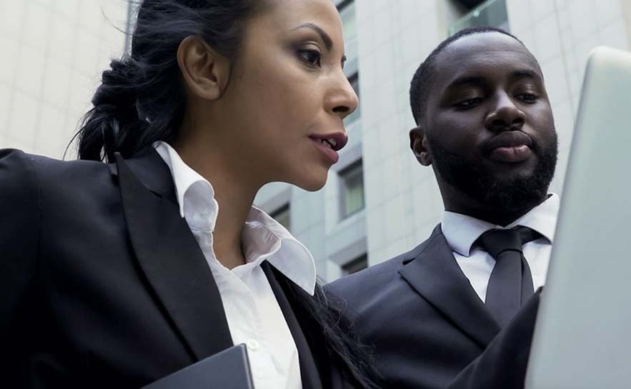 Two individuals in business attire standing close together, looking at a laptop or screen.