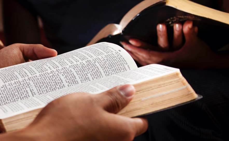 Two sets of hands holding an open Bible.