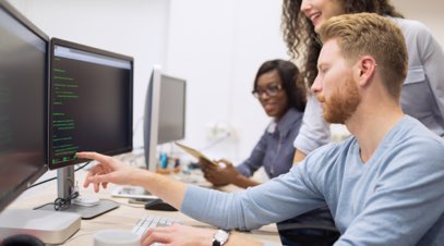 Information technology professional reviewing code on computer screen with team-alt-text