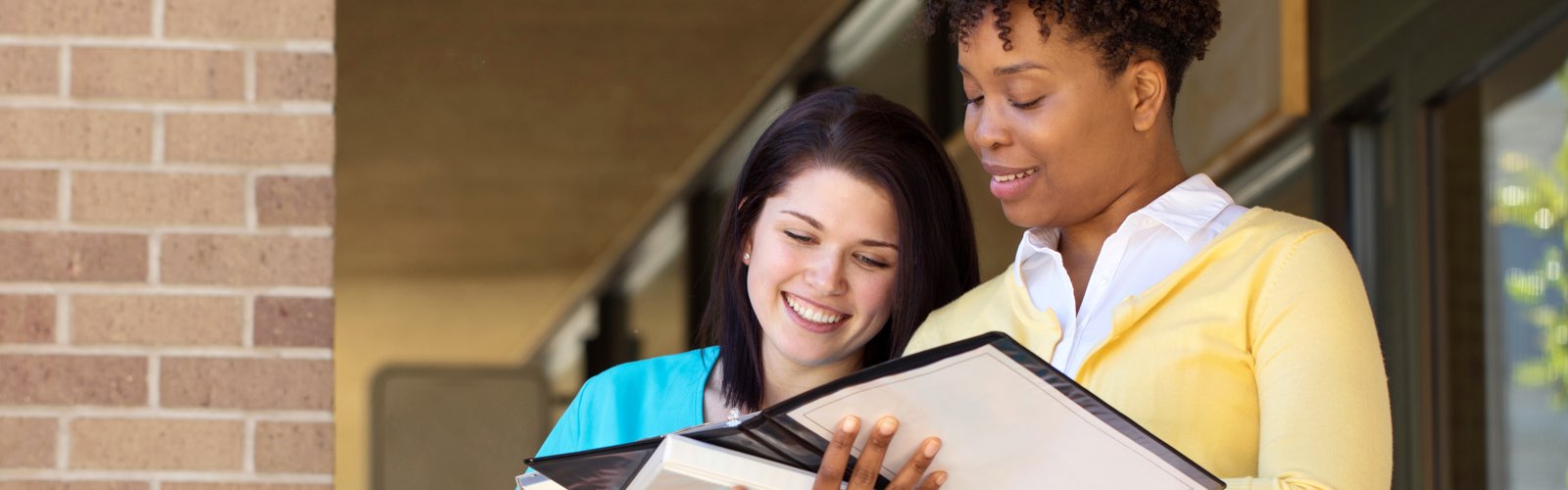 Two female nursing students smiling and looking at notebook