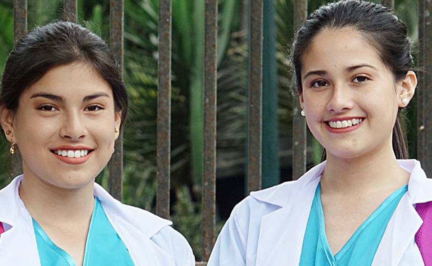 Two young women in scrubs and medical coats.