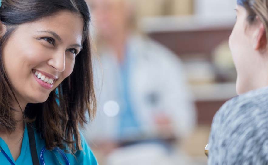 Smiling woman in scrubs looking at another individual.
