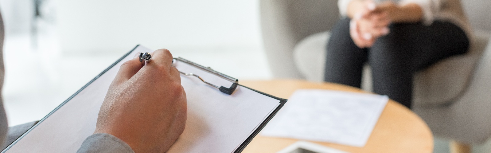a person's hand resting on a clipboard and is sitting across another person