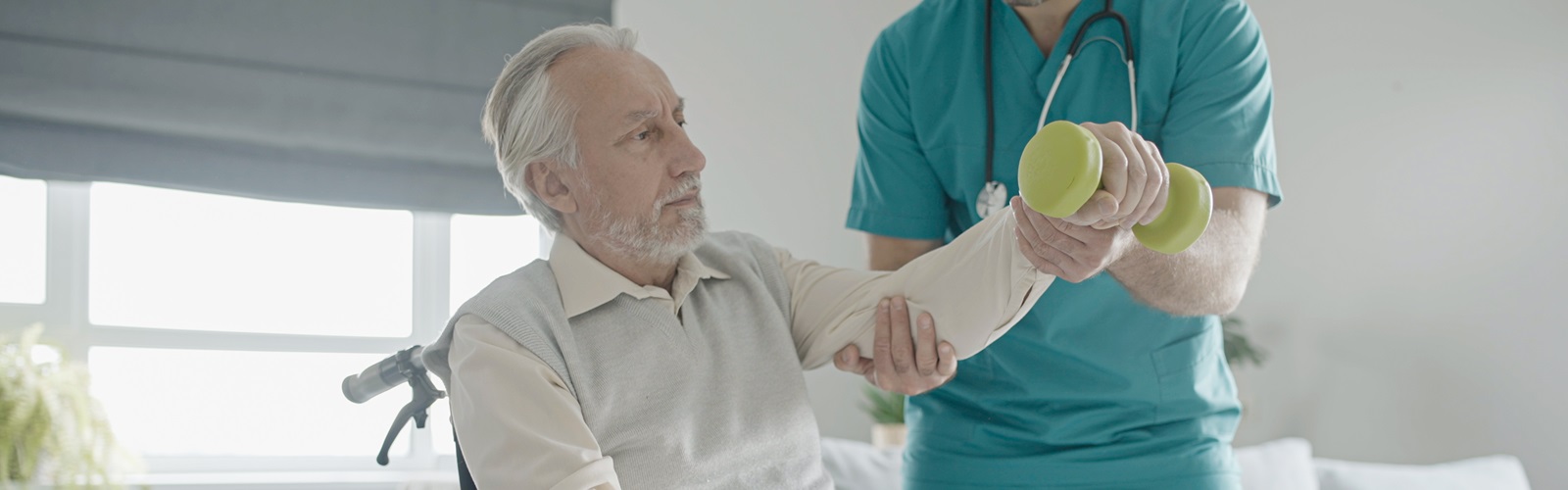 older gentleman sitting in a wheelchair receiving help with weight lifting from physical therapy assistant