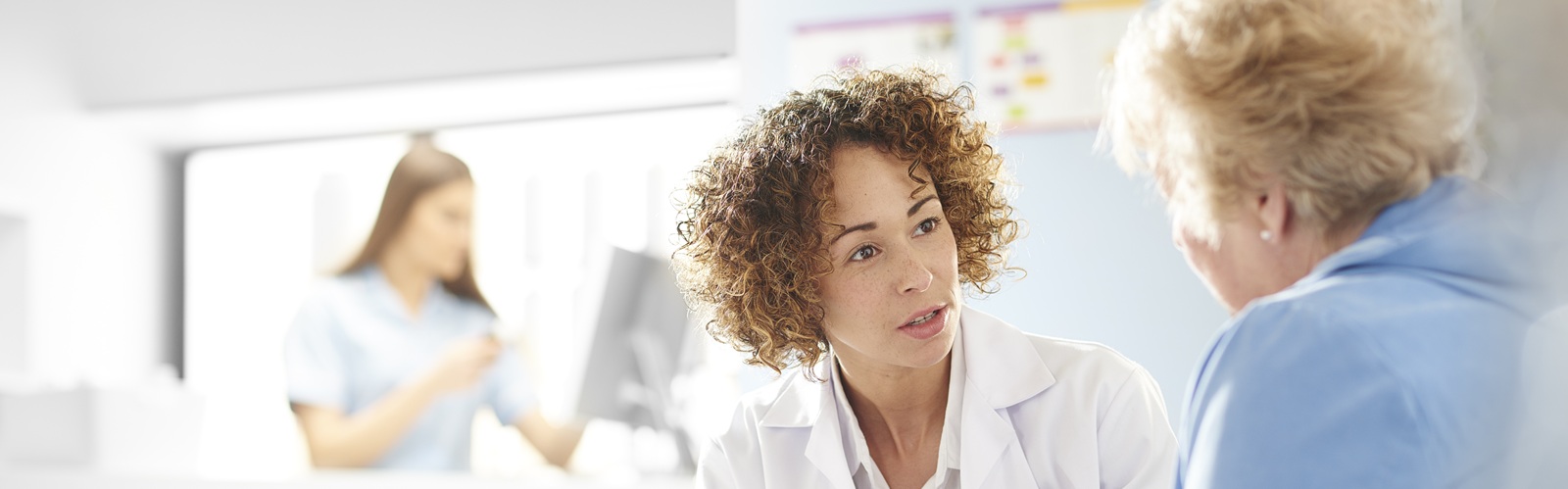 pharmacist in a white coat speaking with an older female patient in a blue coat in a hospital