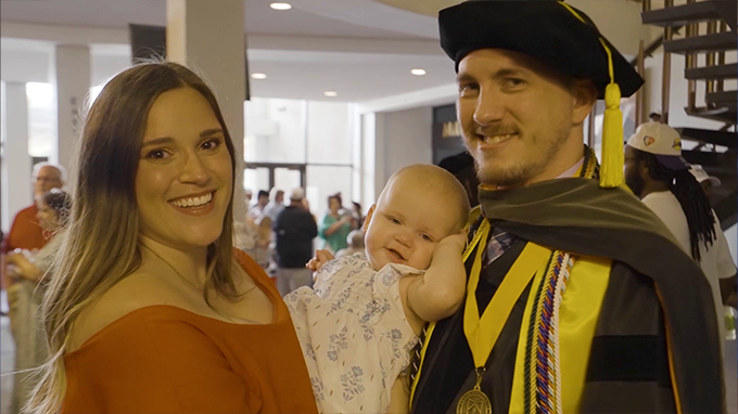 man, wife and baby at his graduation ceremony